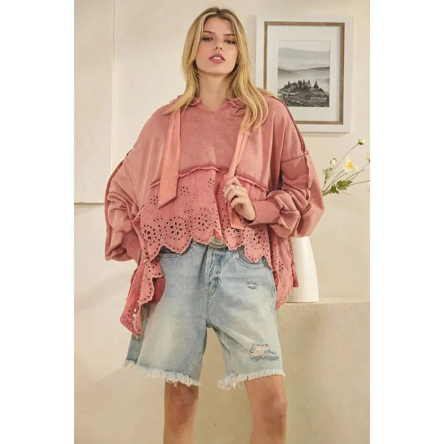 Woman wearing a pink sweater with eyelet details and denim shorts indoors.
