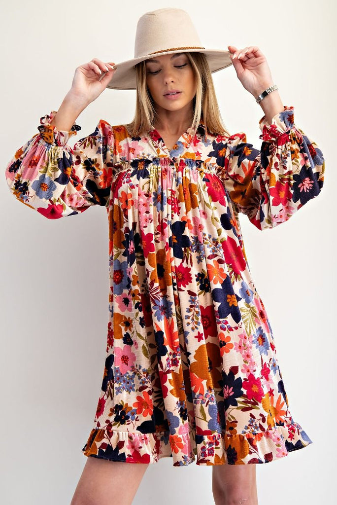 Woman wearing a multicolor floral velvet dress with collared v-neckline, ruffled cuffs, and flowy silhouette styled with ankle boots.