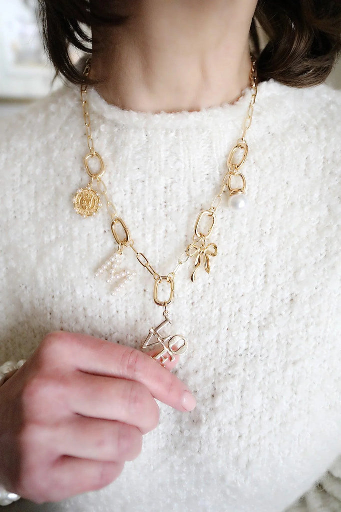 Gold necklace with floral and bow designs worn by a person in a white sweater.