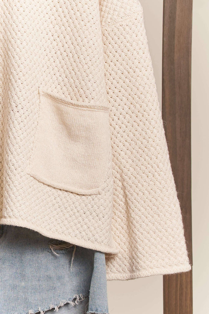 Close-up of a textured beige sweater with a pocket, worn over light blue jeans.