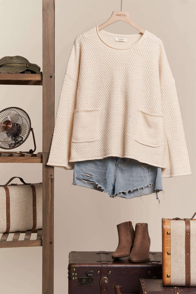 Beige sweater, denim shorts, and brown boots on a hanger with vintage suitcases and fan in the background.