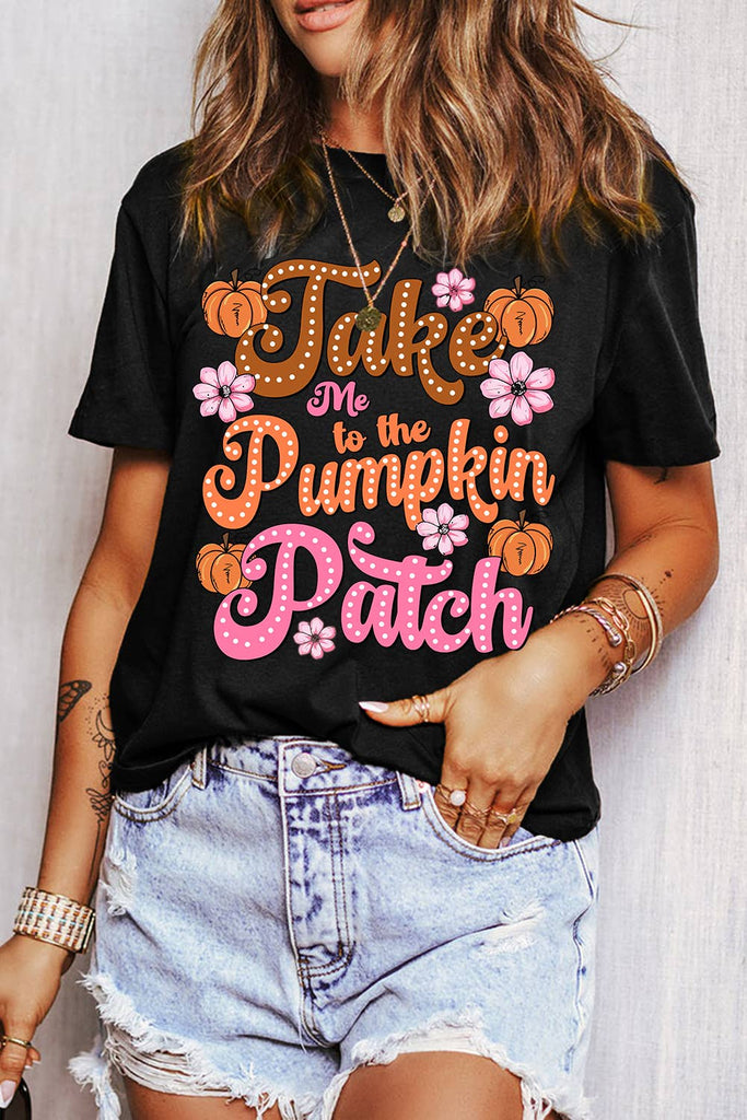 Woman wearing a black graphic tee with “Take Me to the Pumpkin Patch” slogan and floral pumpkin design, styled with distressed denim shorts.